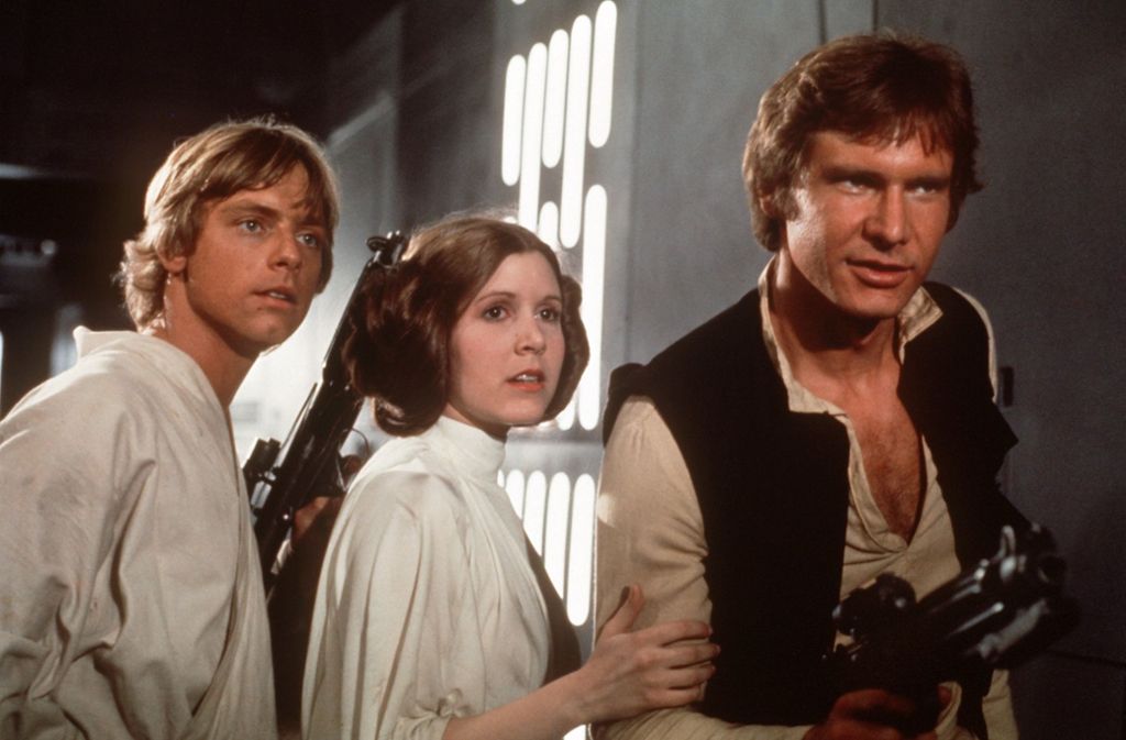 Captain Han Solo (rechts alias Harrison Ford) ist ein Hauptakteur im „Star-Wars“-Universum. Er gehört zum Volk der Correlianer. Auf dem umgebauten Frachter „Millenium Falken“ kämpft er auf Seiten der Rebellen-Allianz mit dem Jedi-Ritter Luke Skywalker (links, Mark Hamill) und Prinzessin Leia (Mitte, Carrie Fisher, 1956-2016) gegen das Imperium unter Lord Darth Vader.