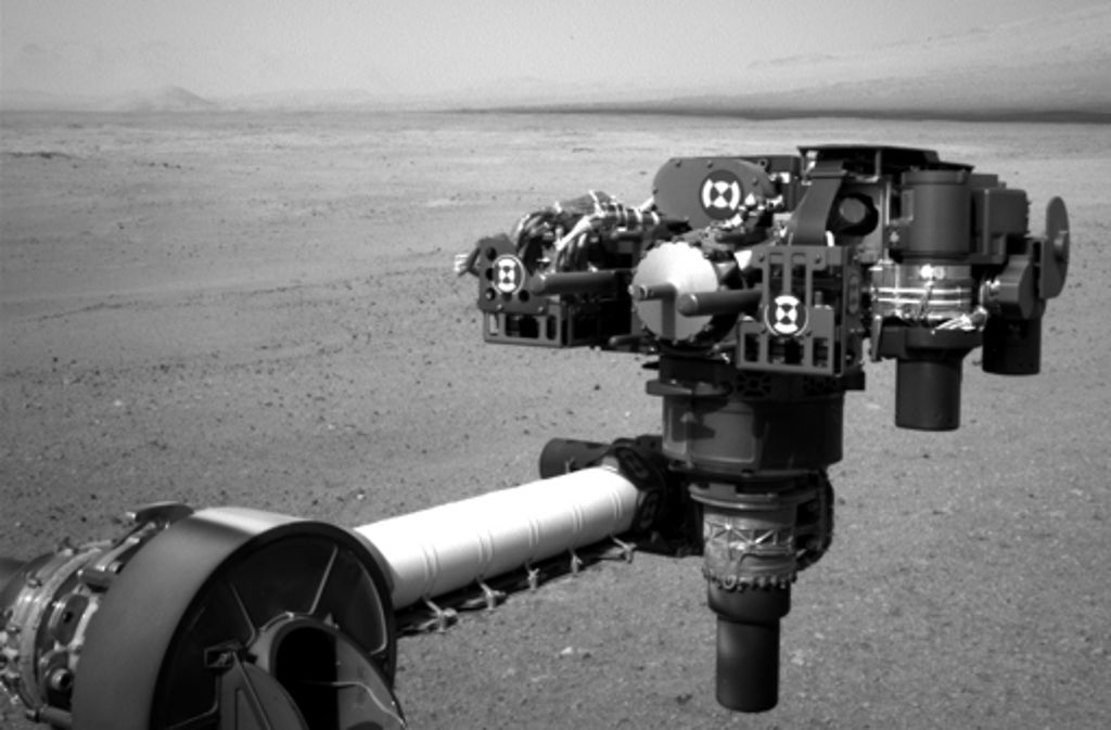 Am Ende eines Roboterarms von Curiosity sind eine Reihe von Geräten montiert: Bohrer und Messinstrumente. Das Foto des Arms stammt von einer kleinen Navigationskamera und ist deshalb nur schwarz-weiß.