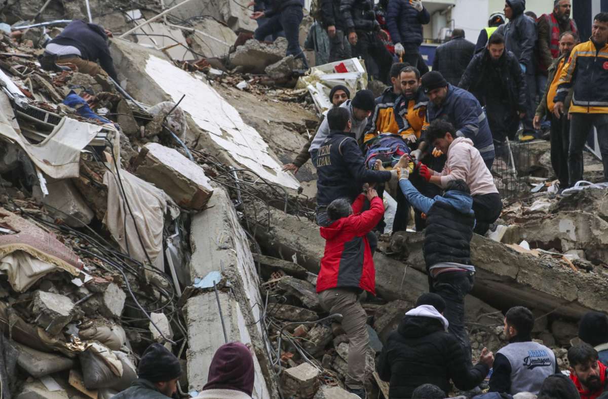 Menschen und Rettungskräfte bergen in der türkischen Stadt Adana eine Person auf einer Bahre aus einem eingestürzten Gebäude. Ein starkes Beben hat im Südosten der Türkei und in Syrien mehrere Gebäude zum Einsturz gebracht, und es werden viele hundert Opfer befürchtet. Foto: Elifaysenurbay/IHA/AP//pa