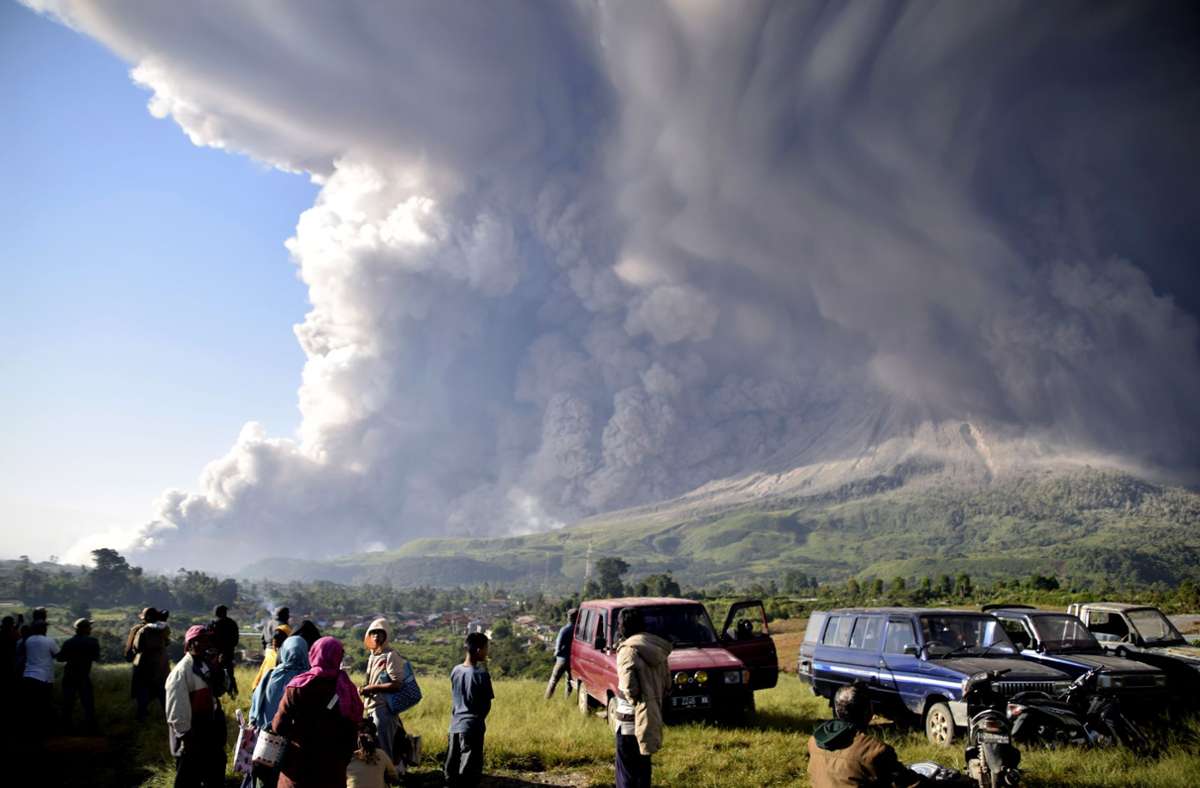 Menschen beobachten eine Eruption des Vulkans Sinabung. Der knapp 2500 Meter hohe Vulkan ist einer von mehr als 120 aktiven Vulkanen in Indonesien.