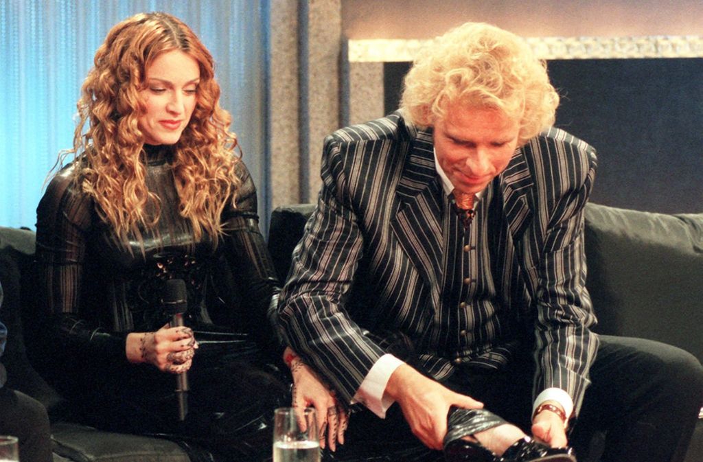 1998: Thomas Gottschalk bewundert bei Gummibärchen und Tafelwasser während der Fernsehsendung „Wetten, dass..?“ die Schuhmode von Madonna.