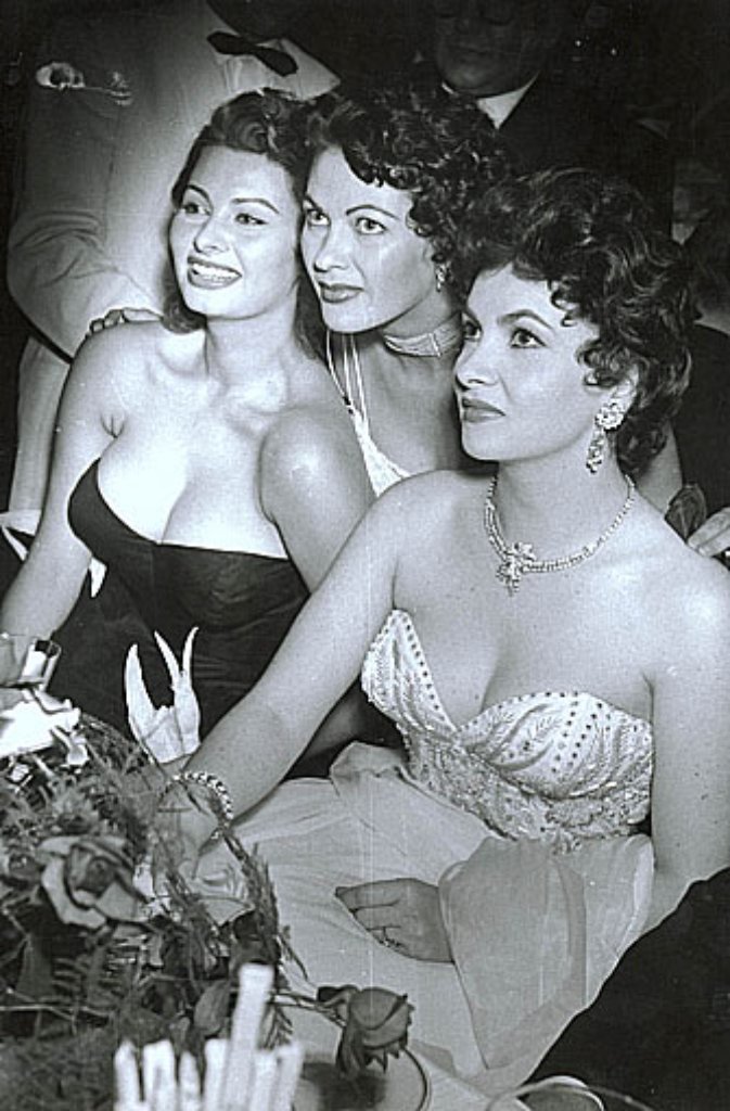 1954: Treffen der Gigantinnen - die italienischen Erzfeindinnen Sophia Loren (links) und Gina Lollobrigida (rechts) lächeln gemeinsam in die Kamera. Als Puffer fungiert die US-Schauspielerin Yvonne de Carlo (Mitte).