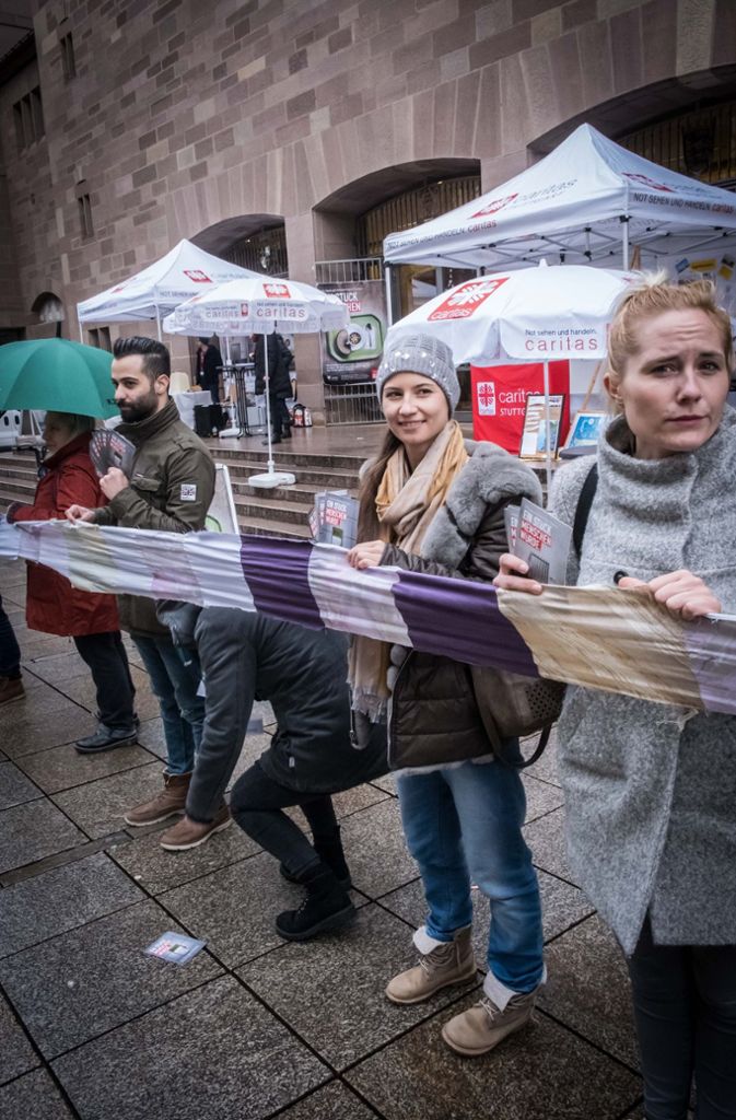 Mitwirkende der Caritas-Kampagne halten den Schal auf der Königstraße hoch.