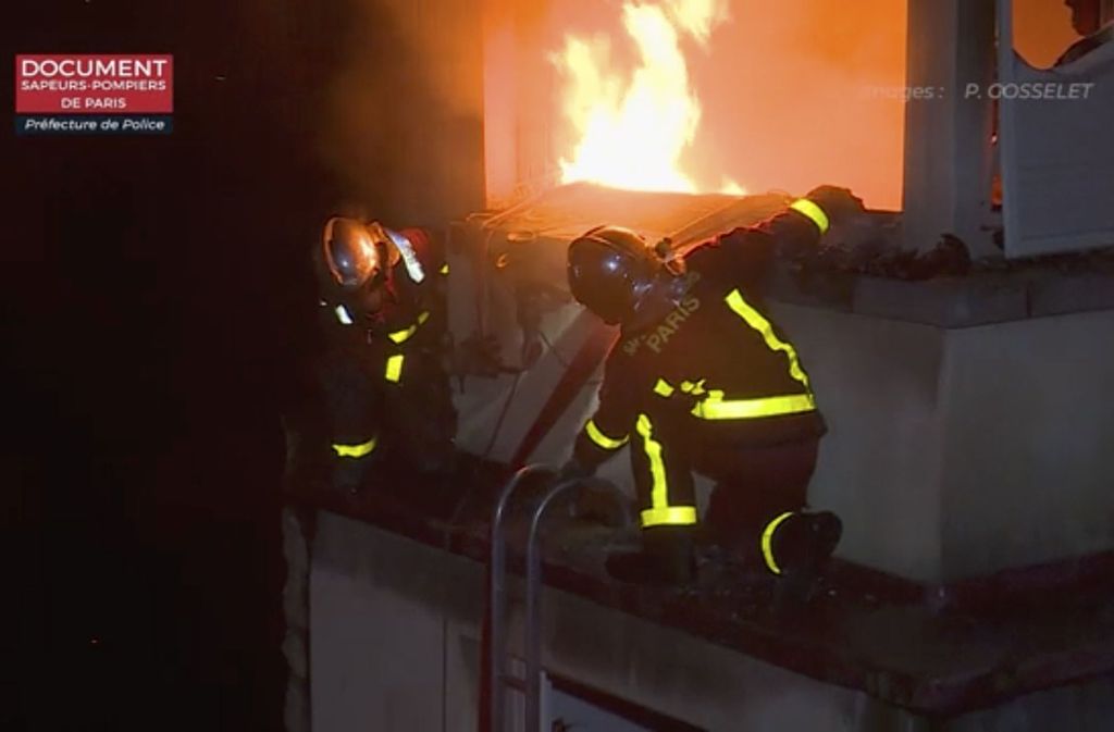 Das Videostandbild zeigt Feuerwehrleute im Einsatz an einem brennenden Mehrfamilienhaus.