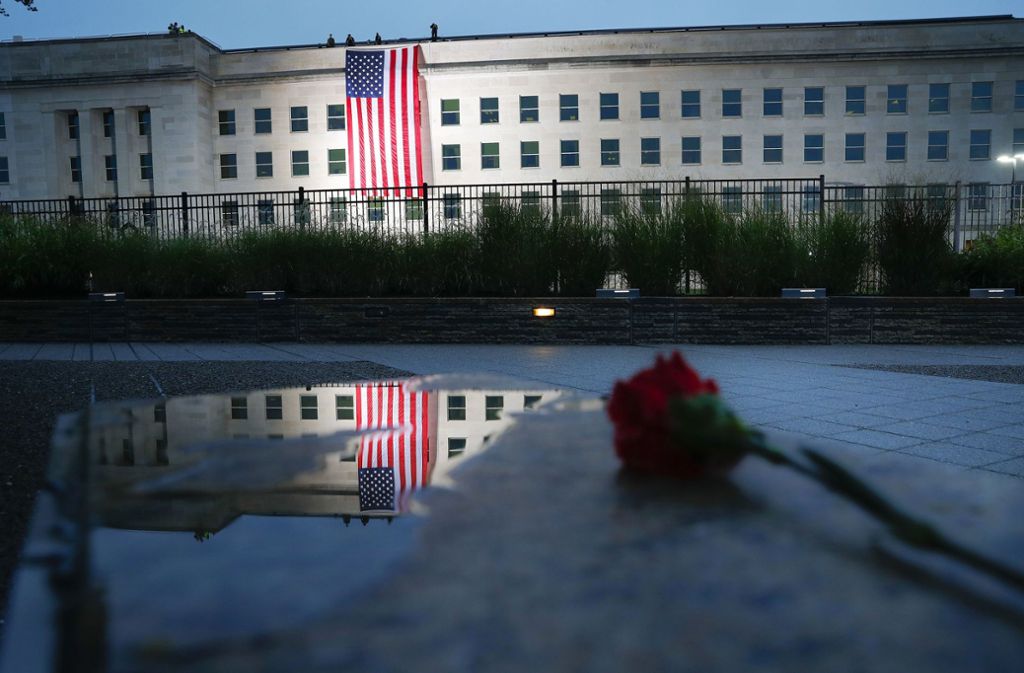 Zum Jahrestag der Anschläge vom 11. September wird zum Sonnenaufgang vom Dach des Pentagons eine US-amerikanische Flagge heruntergelassen, die sich in einer Pfütze spiegelt, neben der eine rote Rose liegt.