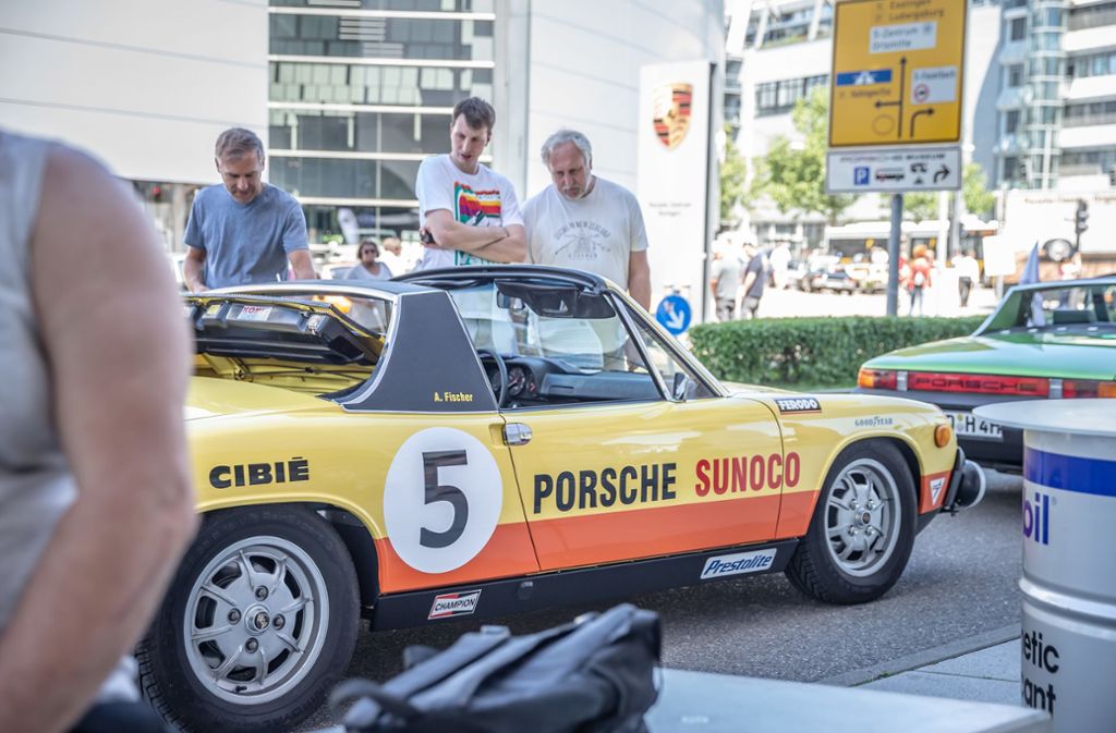 Besucher schauen sich einen Porsche an, welcher mit vielen anderen vor dem Museum geparkt wurde.
