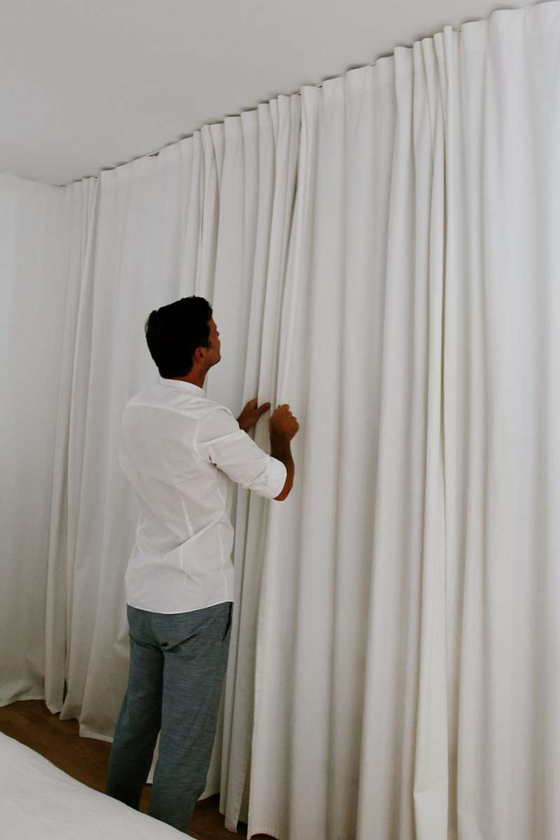 Um den minimalistischen Look zu erreichen, wurde im Schlafzimmer der offene Kleiderschrank hinter weißen Vorhängen versteckt. Diese dienen gleichzeitig auch als Schutz vor Sonnenlicht am Fenster. 