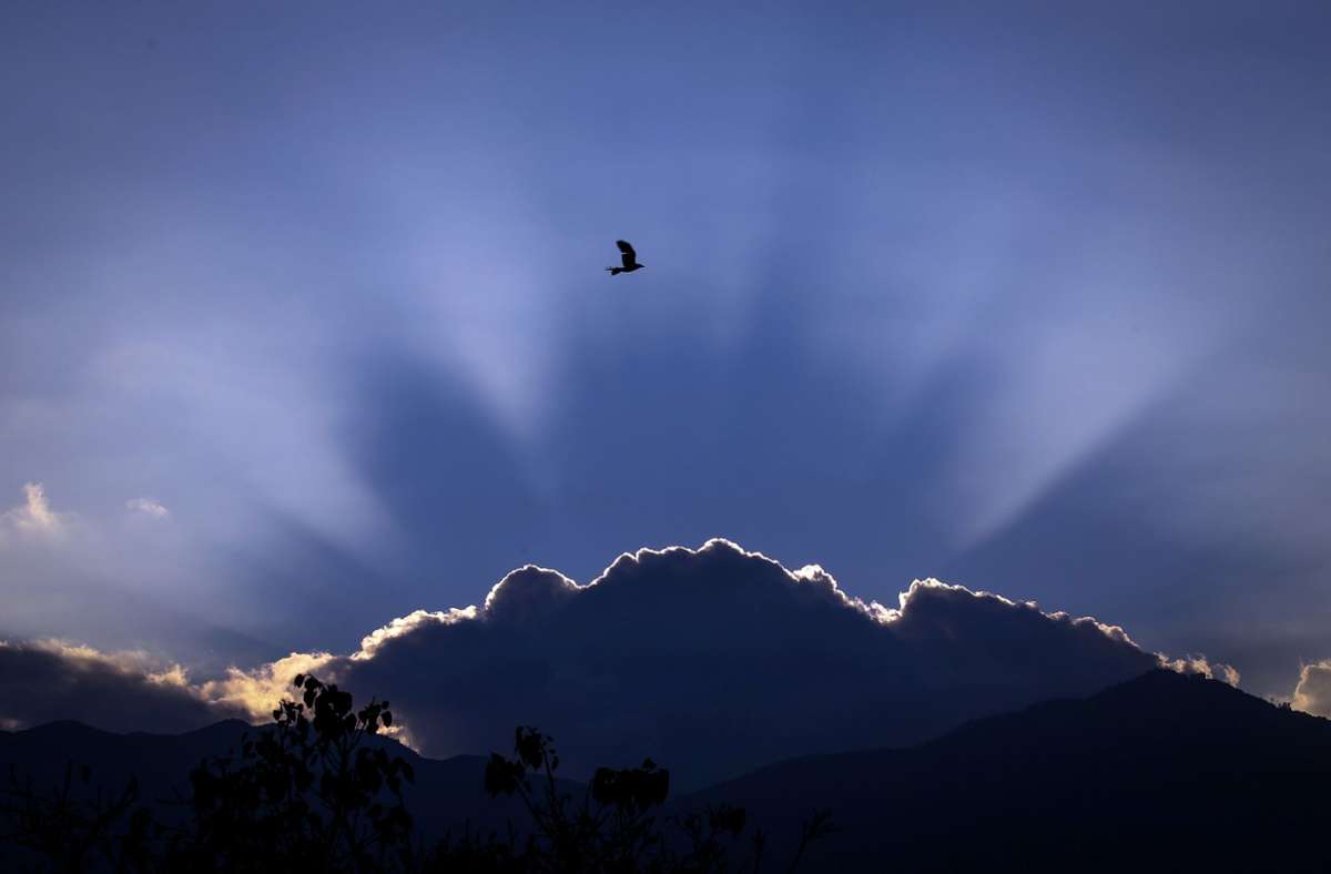 Nepal, Kathmandu: Ein Vogel fliegt am Himmel, während die Sonne hinter einer Wolke am Horizont das letzte mal im Jahr 2021 untergeht.