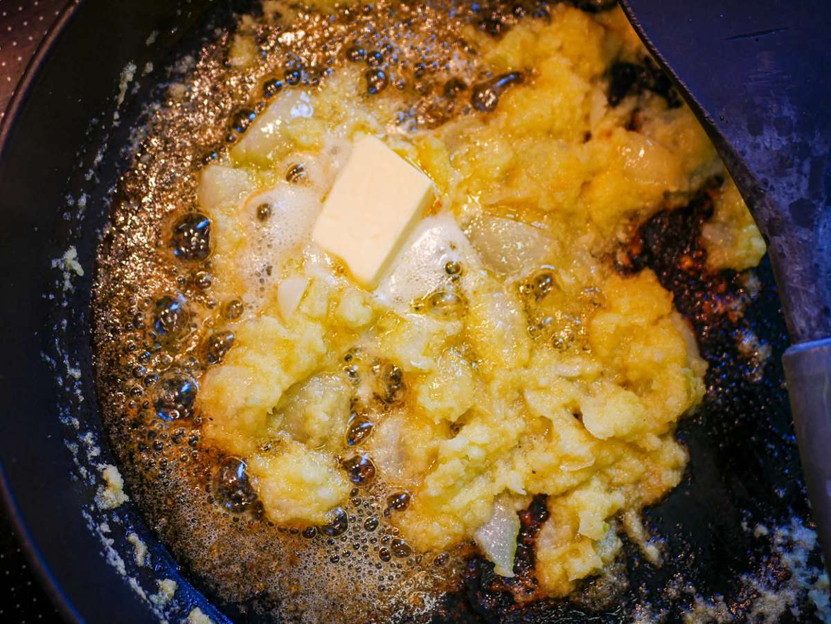 In einer tiefen Pfanne Öl erhitzen und die Zwiebeln darin zwei Minuten auf mittlere Hitze anschwitzen. Knoblauch-Ingwerpaste dazugeben und weitere 30 Sekunden anschwitzen.