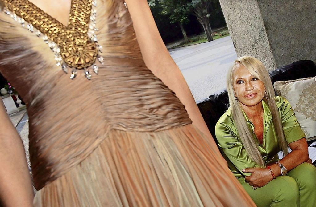 Typisch Versace: viel Gold und Glitzer, seidige Stoffe, gewagte Schnitte. Hier blickt Donatella Versace zufrieden auf einen ihrer Entwürfe. Das Foto stammt von 2005, aus einer Zeit, als es mit dem Modeunternehmen langsam wieder bergauf ging.