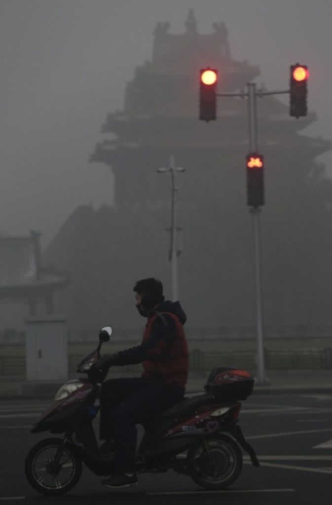 Mit Atemmaske und Roller ist ein junger Mann auf den Luft verschmutzten Straßen Pekings unterwegs.