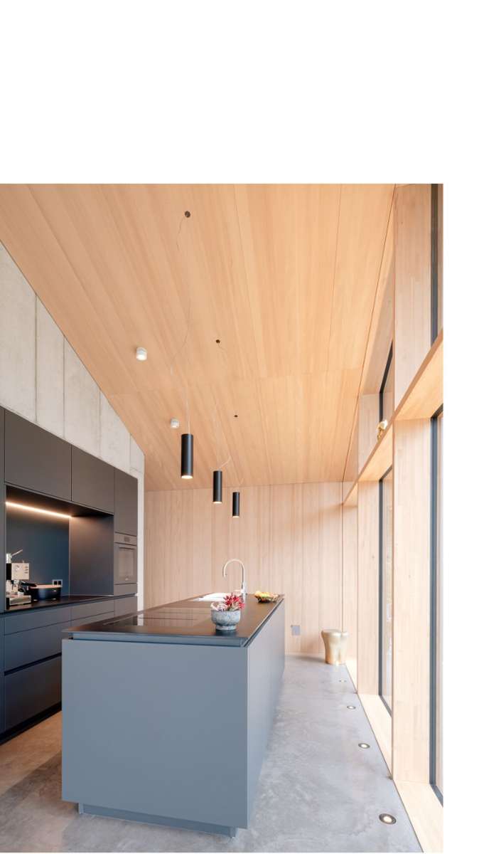 Die Materialien Holz und Beton prägen auch die Atmosphäre im Küchenbereich. Auf den hellgrauen Sichtbetonflächen zeichnet sich das regelhafte Muster der Schalplatten ab.