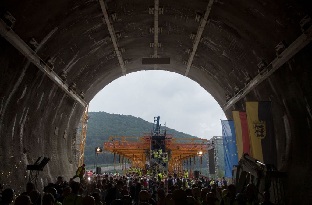Tunnelarbeiter und Besucher der Durchschlagsfeier stehen nach dem Durchschlag im Boßlertunnel, im Hintergrund ist ein Gerüst der sich im Bau befindlichen Filstalbrücke zu sehen.