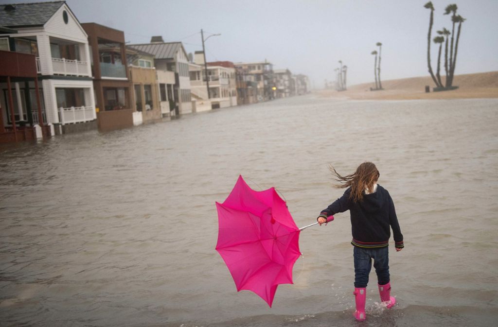 Ein 6-jähriges Mädchen watet in Seal Beach, Kalifornien (USA) mit einem pinken Regenschirm in der Hand durch über die Ufer getretenes Wasser am Pier der Stadt.