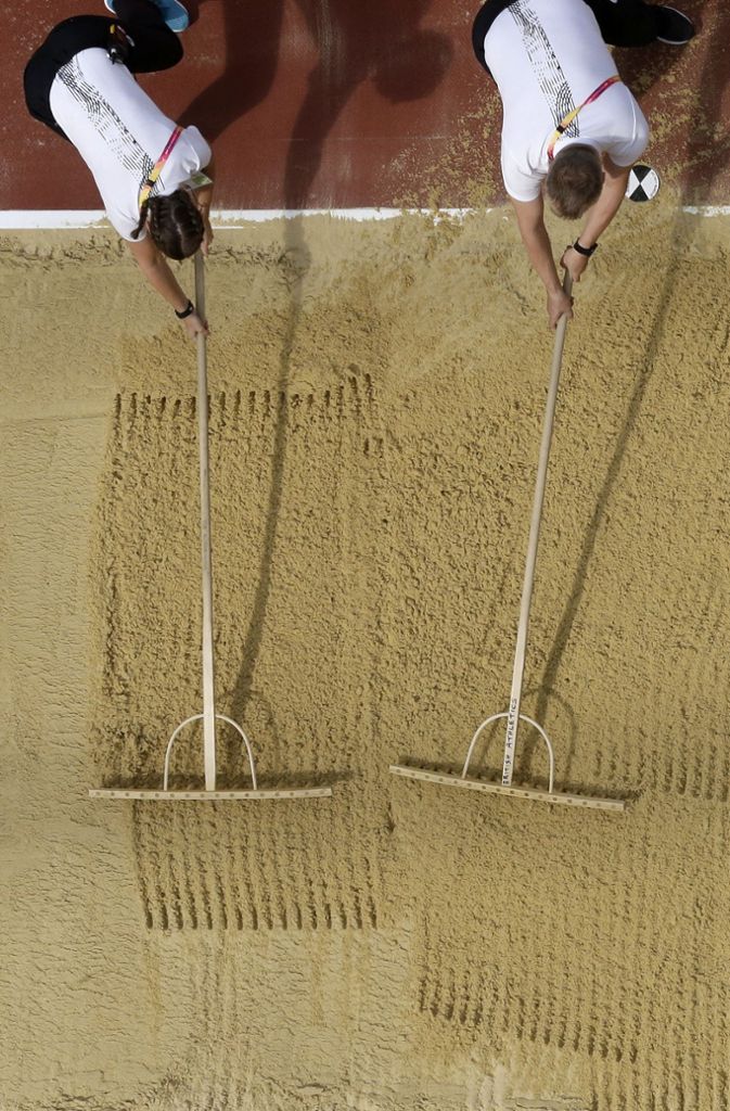 Helfer harken während der Qualifikation im Dreisprung den Sand in der Grube