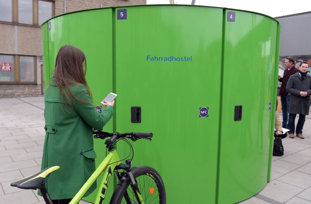 Eine Fahrradfahrerin bucht vor dem Bahnhof Lichtenberg in Berlin über eine App auf ihrem Smartphone einen Platz in einer abschließbaren Fahrrad-Abstellbox.