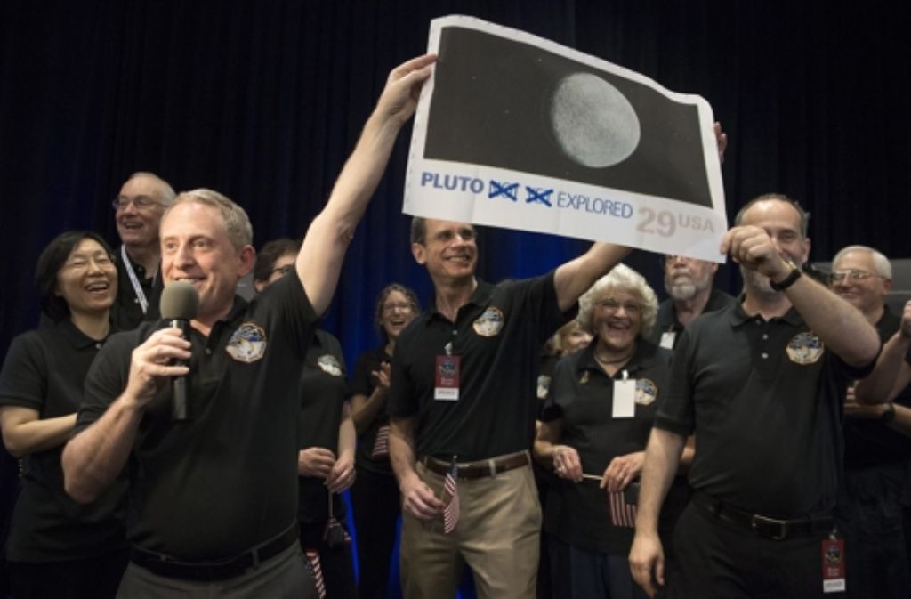 Das New-Horizons-Team hat Geschichte geschrieben. Der wissenschaftliche Leiter Alan Stern (vorne links) hält die Großkopie einer 29-Cent-Briefmarke hoch, auf der die Worte „not yet“ („noch nicht“) durchgekreuzt sind. Der Pluto ist nun erkundet – als letzter, nunja, Planet des Sonnensystems.