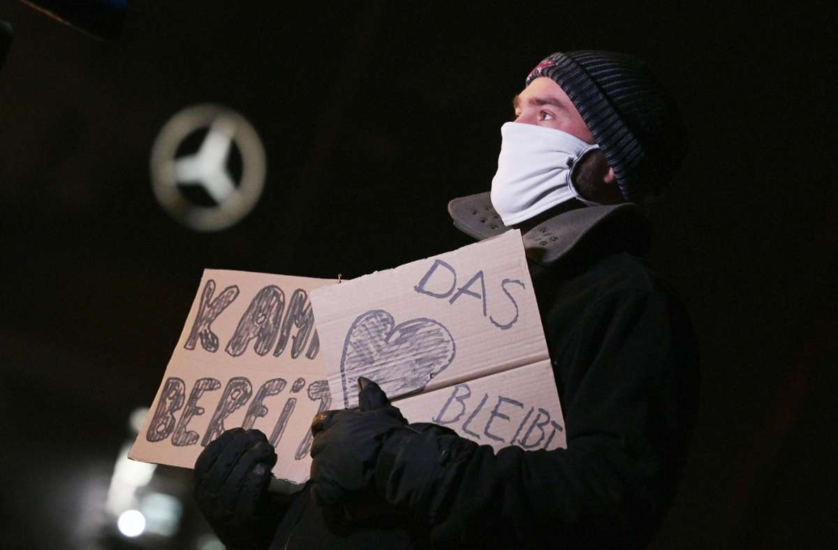 Ein Mitarbeiter der Daimler AG steht am Rande einer Protestaktion des Daimler-Gesamtbetriebsrats und der IG Metall mit zwei Plakaten vor einem Mercedes-Stern, der auf der Mercedes-Benz Hauptniederlassung zu sehen ist.
