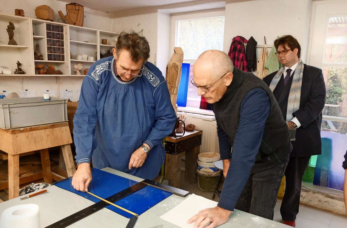 Valentin Saile (li.) zeigt einem Kursteilnehmer an der Freien Kunstschule, wie Glas zugeschnitten wird. Auch Rektor Martin Handschuh (re.) schaut interessiert zu.