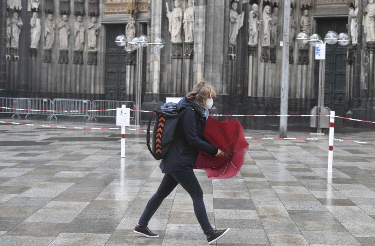 Am Kölner Dom kämpfen Passanten mit ihren Regenschirmen.