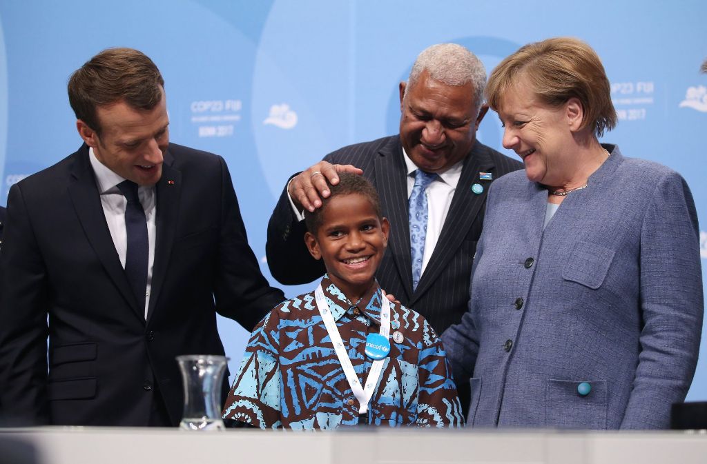 Angela Merkel und der französische Präsident Emmanuel Macron (links)  begrüßen bei der Weltklimakonferenz gemeinsam mit dem Premierminister der Fidschi-Inseln, Frank Bainimarama, einen zwölfjährigen Junge von den Fidschi-Inseln. Foto: dpa