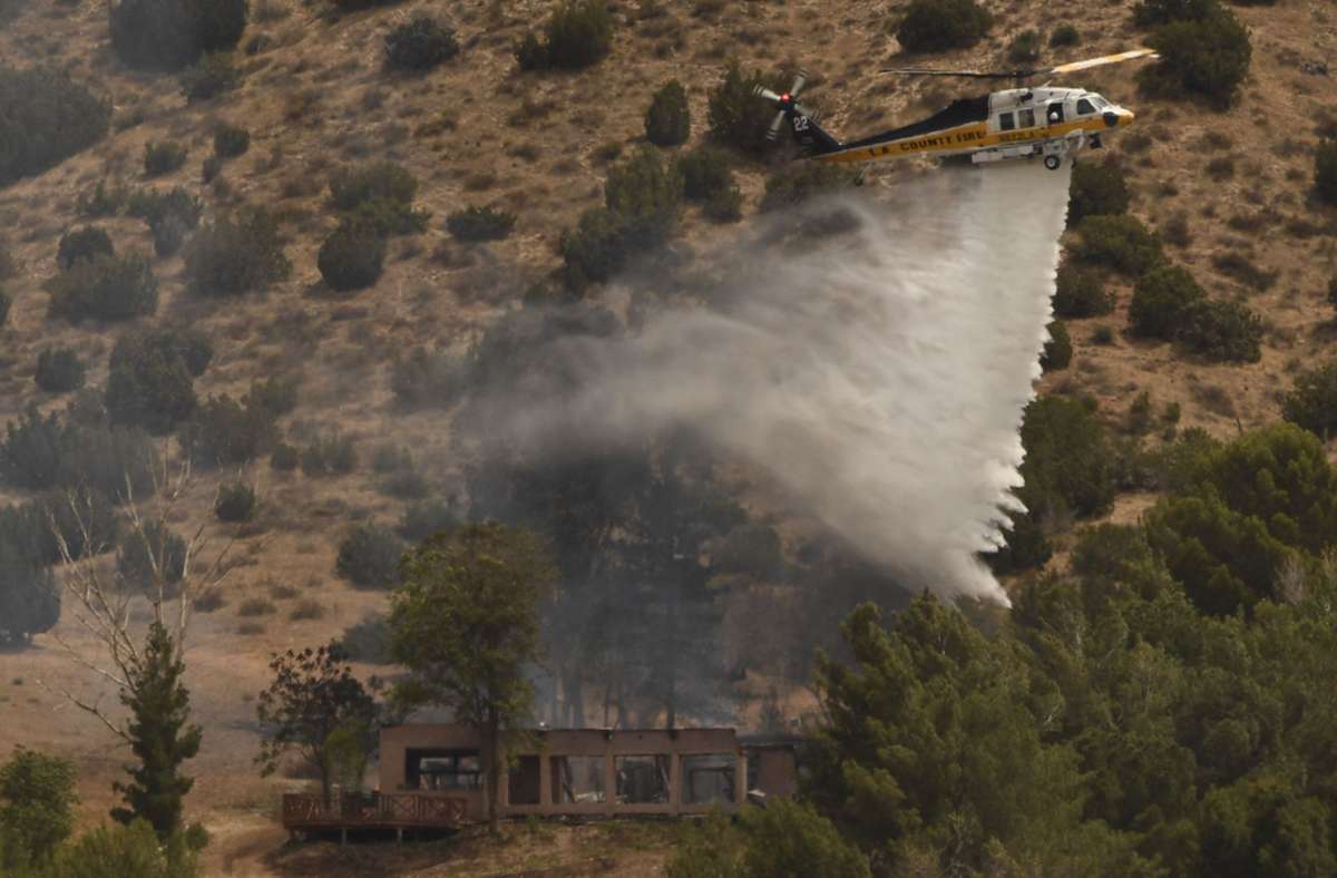 Ein Hubschrauber wirft Wasser über einem brennenden Haus ab.
