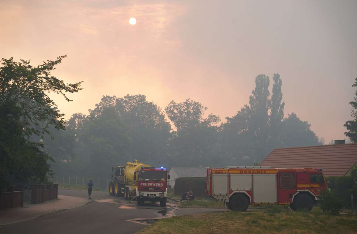 Brandenburg, Beelitz-Heilstätten: Einsatzfahrzeuge der Feuerwehr werden betankt, während dichter Rauch die Sonne verdeckt.
