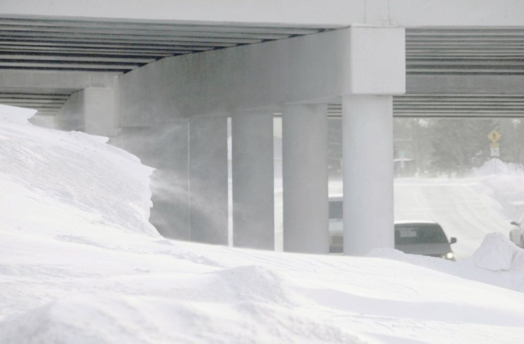 Schnee peitscht in Windböen über die Landschaft während Fahrzeuge eine Unterführung in Fargo durchqueren.