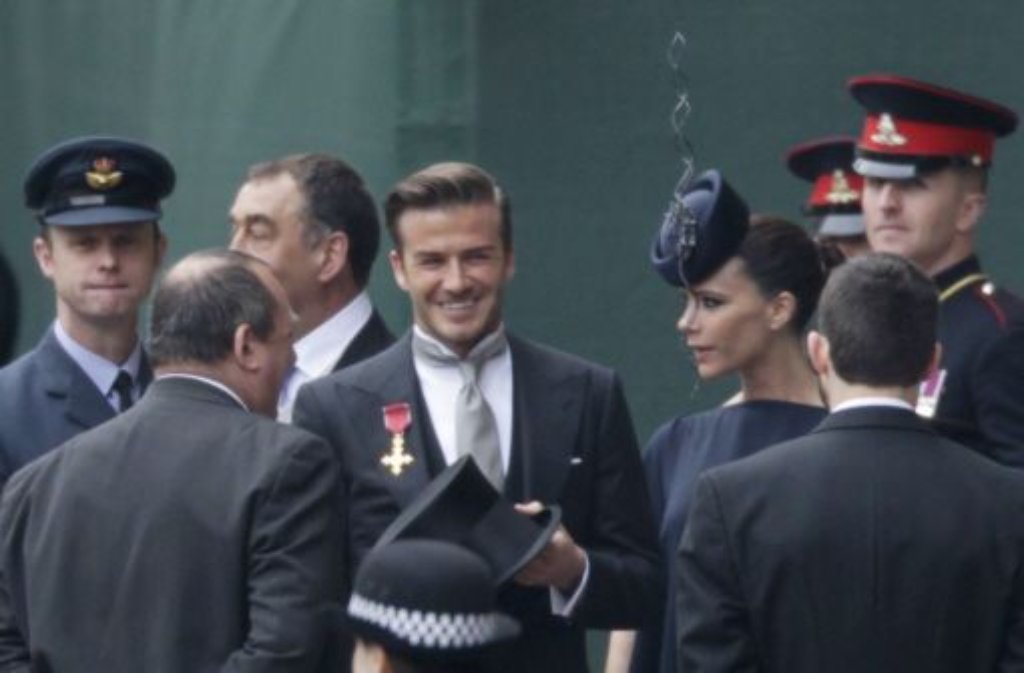 Mit Schmalztolle und Orden zeigt sich David Beckham bestens gelaunt. Seine Frau Victoria blickt etwas finster drein.