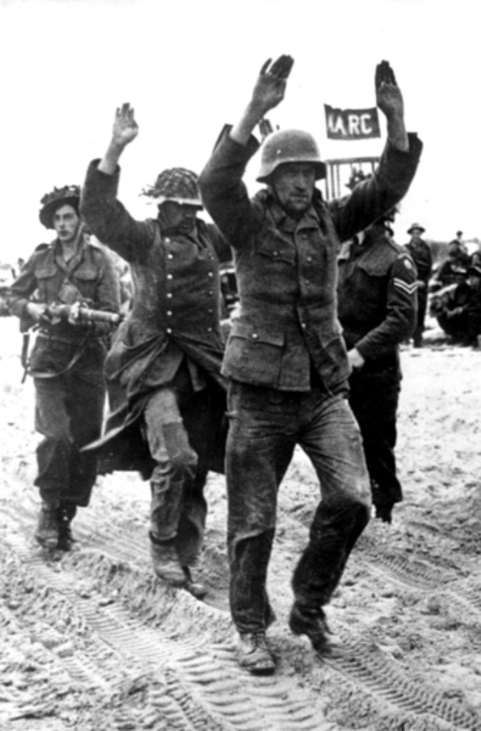 Soldaten der alliierten Truppen führen zwei der ersten deutschen Kriegsgefangenen nach der Landung an der Küste ab. Am 6. Juni 1944 landeten die Alliierten an der Küste der Normandie. Mit der Invasion in Westeuropa begann das Ende des Nationalsozialismus, knapp ein Jahr später, am 8. Mai 1945, endete der Zweite Weltkrieg in Europa mit der Kapitulation Deutschlands.