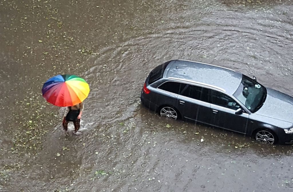Ein Passant versucht sich zumindest von oben mit einem Regenschirm trocken zu halten.