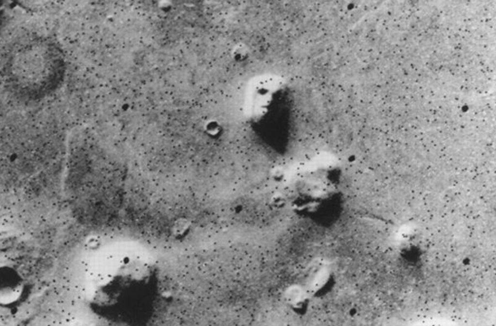 Ein Gesicht auf dem Mars? Die US-amerikanische Raumsonde Viking 1 hat diese Aufnahme der Region Cydonia Mensae 1976 zur Erde gefunkt. Weil die Übertragung nicht perfekt funktionierte, ist das Bild mir schwarzen Punkten übersät. Der Science-Fiction-Film „Mission to Mars“ beruht zum Beispiel auf der Spekulation, dass dieses menschlich anmutende Gesicht ein Zeichen einer außerirdischen Intelligenz sei . . .