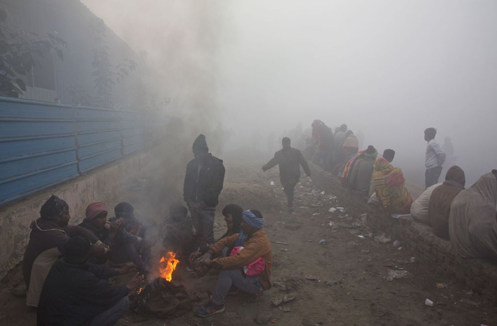 Obdachlose sitzen in Neu-Delhi an einem Lagerfeuer, um sich warm zu halten, während sie bei dichtem Smog auf die Verteilung von kostenlosen Lebensmitteln warten.