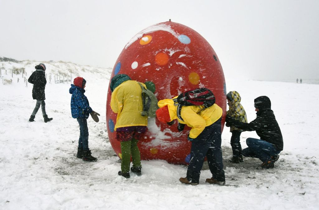 Besucher der Insel Hiddensee bestaunen ein Riesen-Ei, das im Schnee am Strand steht.