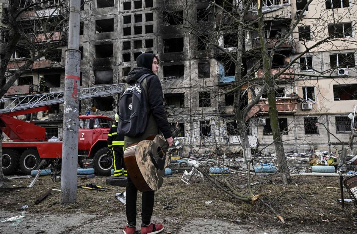 Ebenfalls im betroffenen Stadtteil: Ein junger Mann steht mit seiner Gitarre vor einem zerstörten Wohnhaus. Offenbar starben nach einem russischen Angriff am Montag mehrere Menschen.
