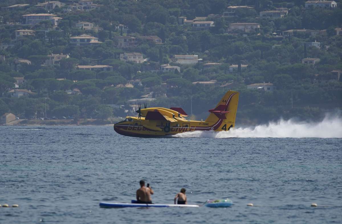 Urlauber baden im Meer, während ein Löschflugzeug seine Tanks mit Wasser auffüllt. Mit einem Großaufgebot kämpft die Feuerwehr in Südfrankreich weiter gegen ausgedehnte Waldbrände.