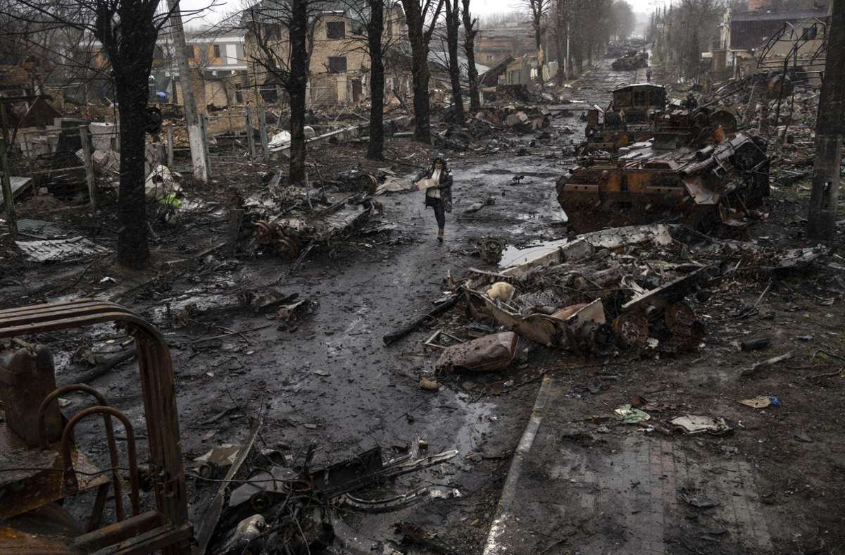 Butscha: Eine Frau geht auf einer Straße, die überseht ist mit zerstörten russischen Militärfahrzeugen.