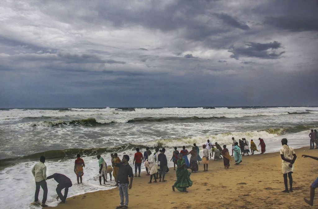 Menschen stehen unter dunklen Wolken an einem Strand im Puri District. Hunderttausende Menschen müssen sich an Indiens Ostküste vor „Fani“ in Sicherheit bringen.