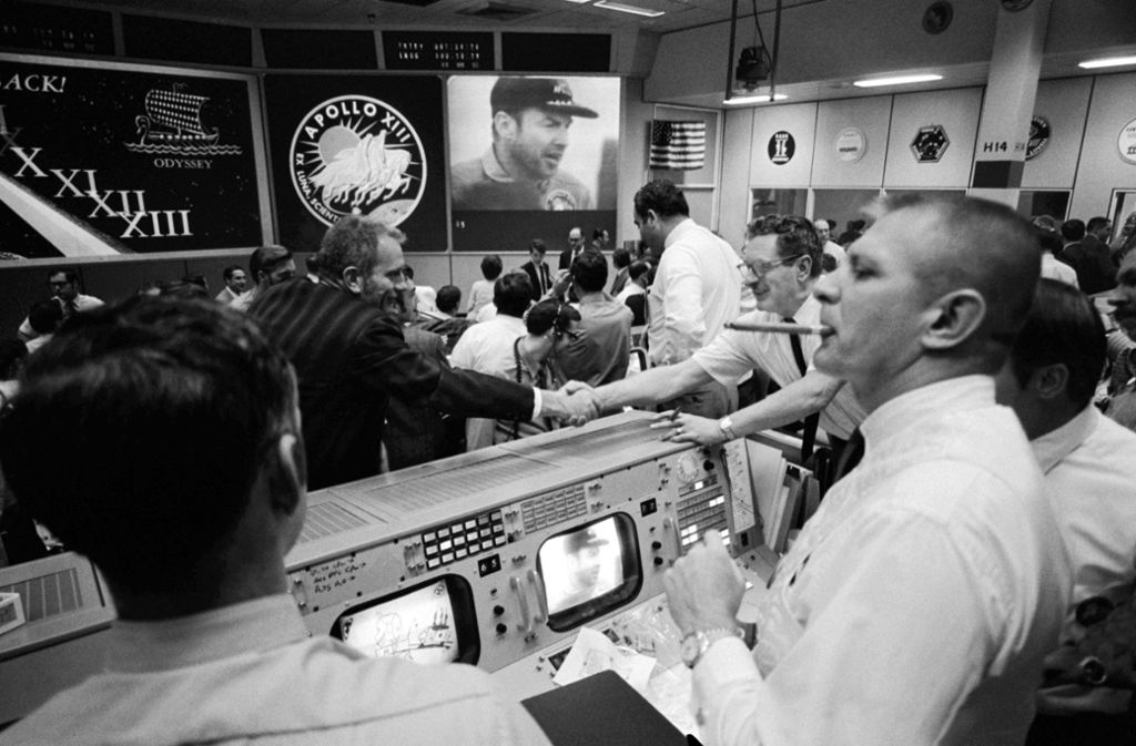 Deke Slayton (im schwarzen Hemd, links von der Mitte), Direktor der Flugbesatzung, und Chester M. Lee geben sich in der Mission Control die Hand, während Rocco Petrone den Apollo-13-Kommandeur Jim Lovell auf dem Bildschirm beobachtet.