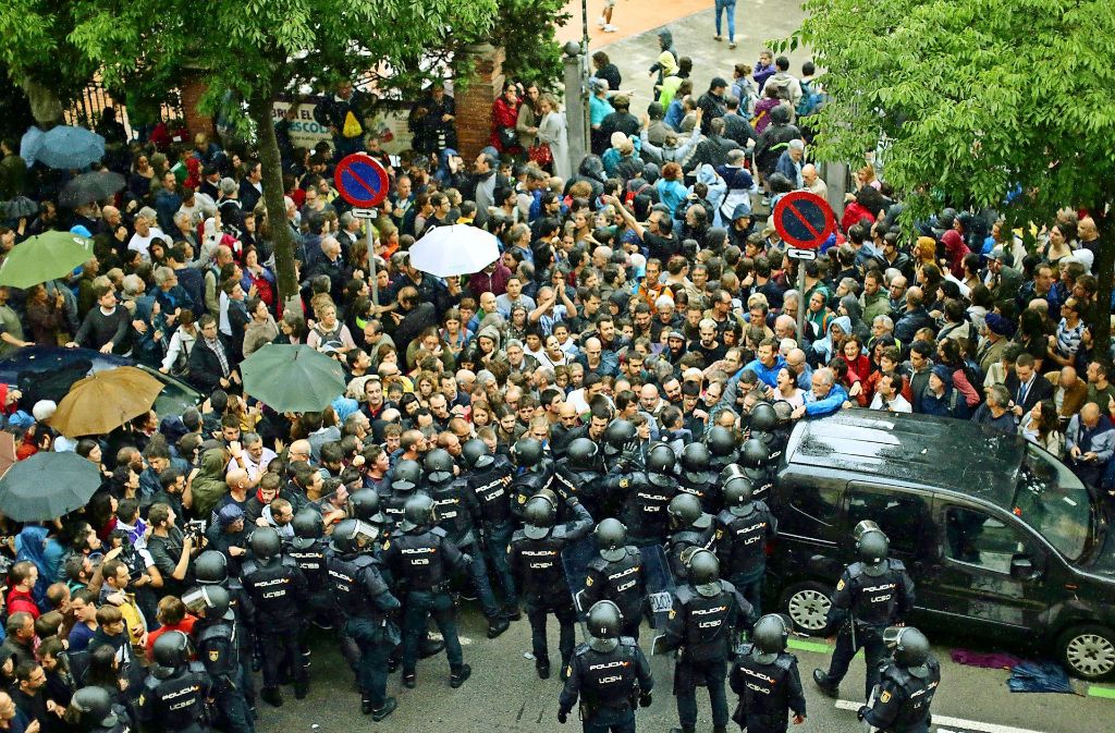 In Barcelona hindern Einheiten der spanischen Nationalpolizei Menschen daran, zum Wahllokal zu gelangen. Vielerorts gelingt die Stimmabgabe dennoch. Separatisten stellen sich in Sant Julia de Ramis mit erhobenen Händen der Polizei entgegen.