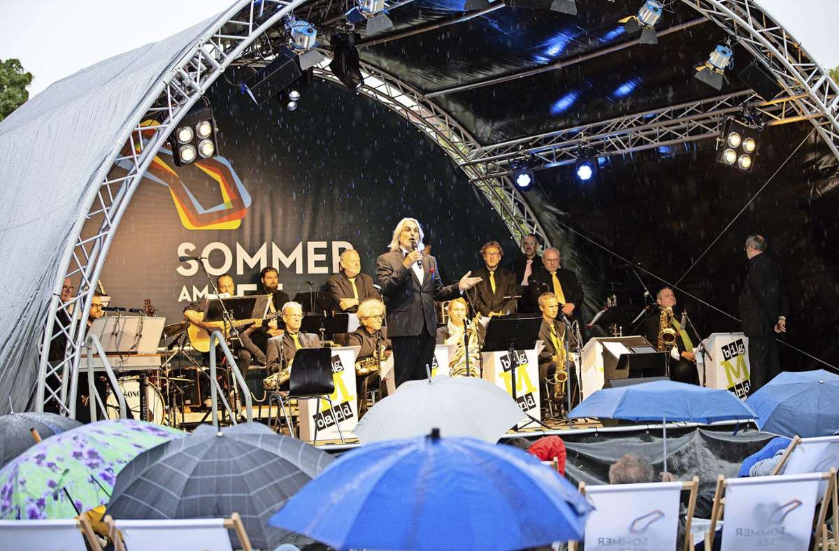 Mit Regenschirmen und Plastikponchos trotzt das Publikum dem Regen beim Sommer-am-See-Auftakt mit Bigband und Sänger Wolfgang Seljé.