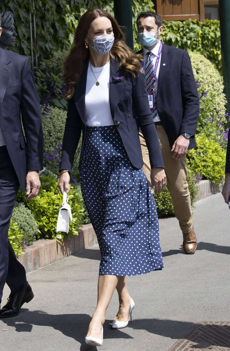 Smart-casual beschreibt diesen Look wohl am besten: Herzogin Kate kombiniert einen dunkelblauen Rock mit weißen Tupfen in Midi-Länge mit weißen Lack-Pumps ...