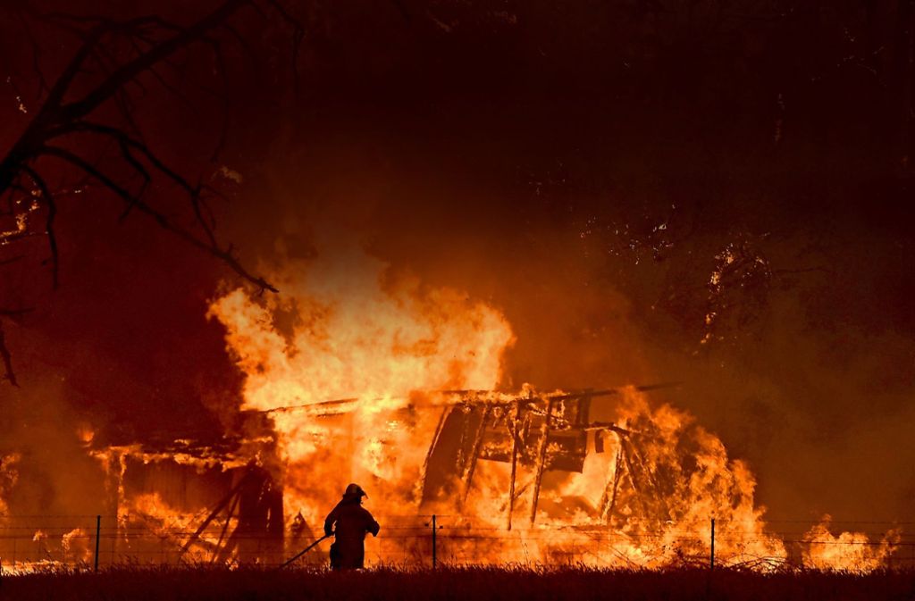 Ein Feuerwehrmann bekämpft in Australien die Flammen eine Buschfeuers, die  ein Gebäude erreicht haben. Foto: AAP/dpa/Dan Himbrechts