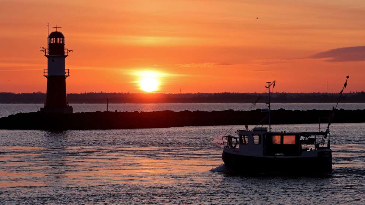 Ein Fischerboot vor der aufgehenden Sonne an der Mole vor Warnemünde: Die bevorstehenden Ostertage versprechen sonniges und relativ mildes Wetter.