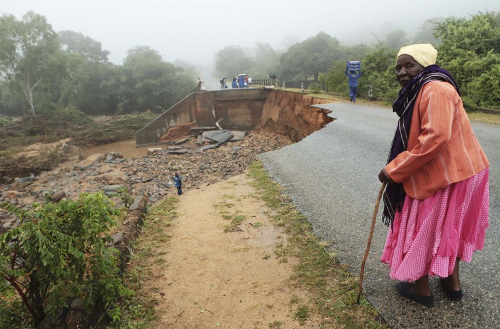 Eine ältere Frau steht neben einer eingestürzten Brücke.