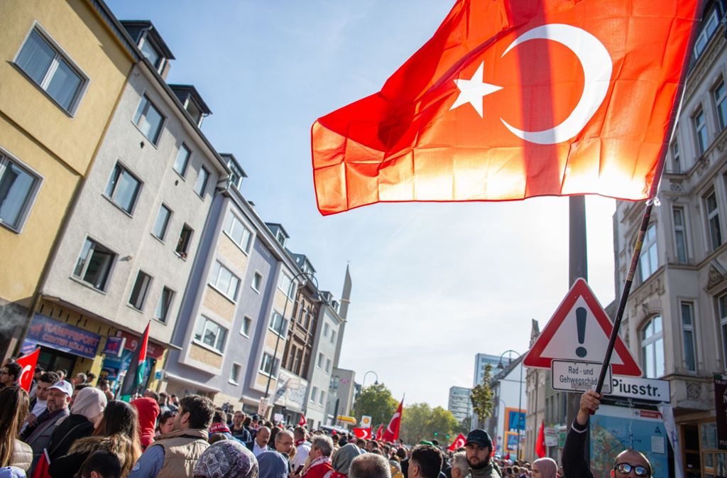 Menschen mit Türkeiflaggen warten an einer Absperrung der Polizei im Umfeld der Ditib-Zentralmoschee, die am Samstag vom türkischen Staatspräsidenten Erdogan eingeweiht werden soll.