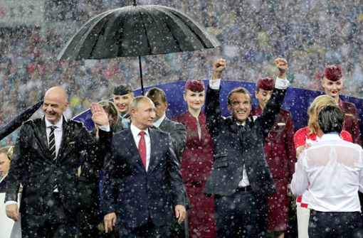Gruppenbild mit Regenschirm: Emmanuel Macron (2.v.r.), Präsident von Frankreich jubelt neben Kolinda Grabar-Kitarovic (verdeckt, rechts), Staatspräsidentin von Kroatien, und Wladimir Putin (2.v.l.), Präsident von Russland, und Gianni Infantino (l), FIFA-Präsident. Foto: dpa