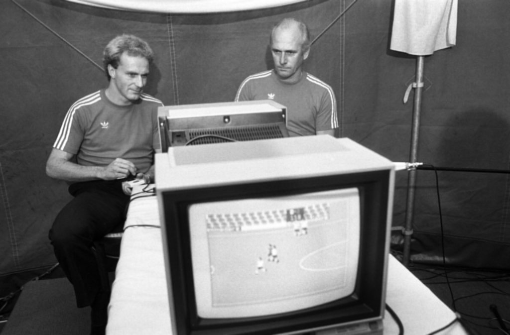FC Bayern-Trainer Udo Lattek (rechts) und sein Stürmer Karl-Heinz Rummenigge sitzen am 20. Oktober 1983 auf der "System 83"-Ausstellung in München an einem Fußball-Computerspiel.