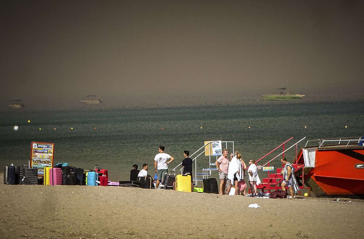 Touristen stehen an einem Strand, wohin sie wegen eines Waldbrandes auf der griechischen Insel Rhodos in Sicherheit gebracht worden sind.