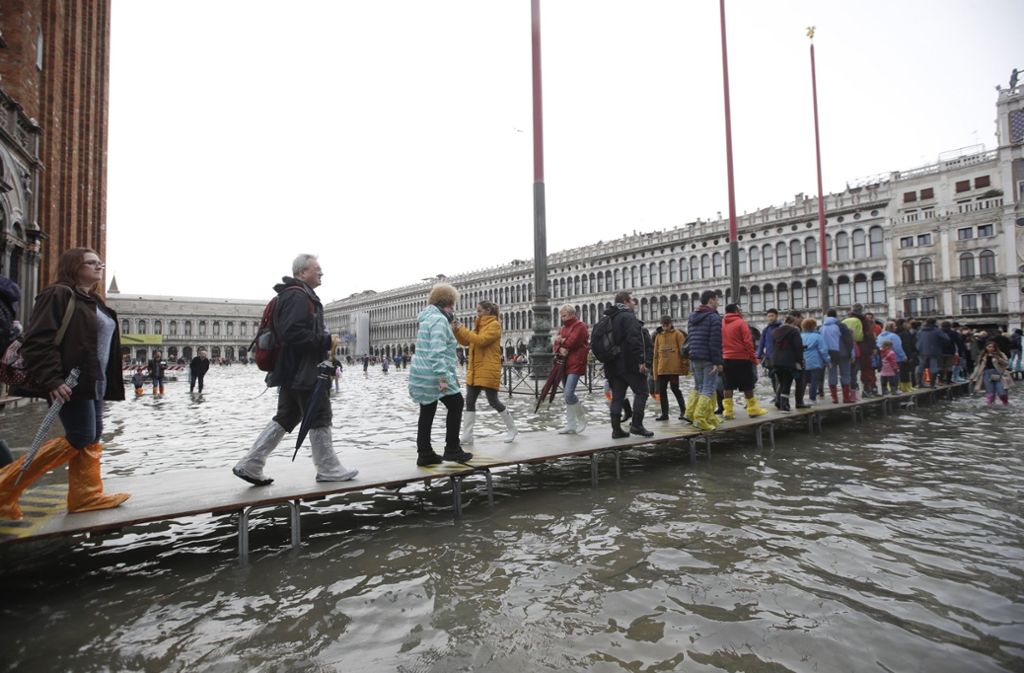 Touristen gehen auf einem improvisierten Holzsteg über den überfluteten Markusplatz.